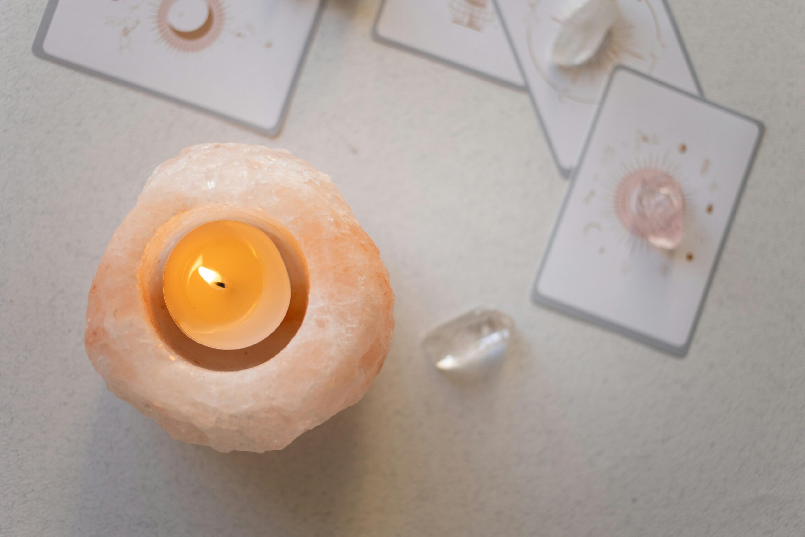 Himalayan salt candle holder with lit tealight surrounded by healing crystals and tarot cards for a spiritual ambiance.